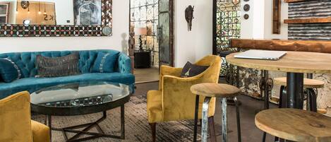 A modern living room with a blue sofa, yellow armchairs, a glass coffee table, and a wooden dining table with bar stools.