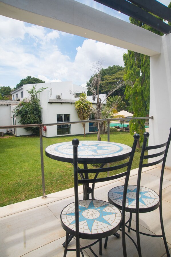 Une terrasse avec une table ronde et des chaises, un bâtiment blanc en arrière-plan et un ciel dégagé.