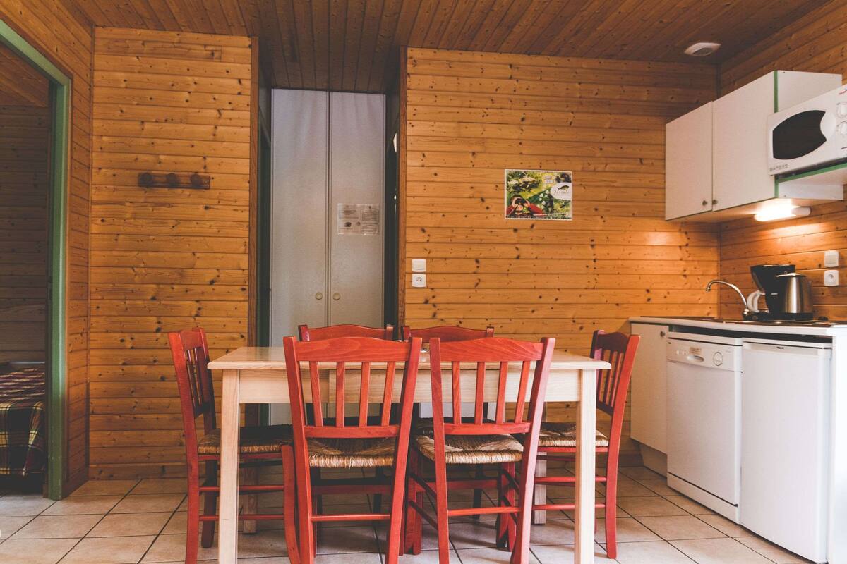 A wooden interior with a dining table and chairs, a kitchen area with a microwave, and a white door.