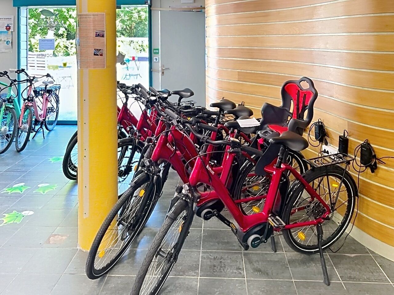 A bike rental station with multiple bicycles, a yellow pillar, and a wooden wall.