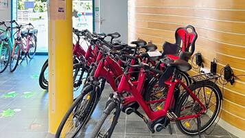 A bike rental station with multiple bicycles, a yellow pillar, and a wooden wall.