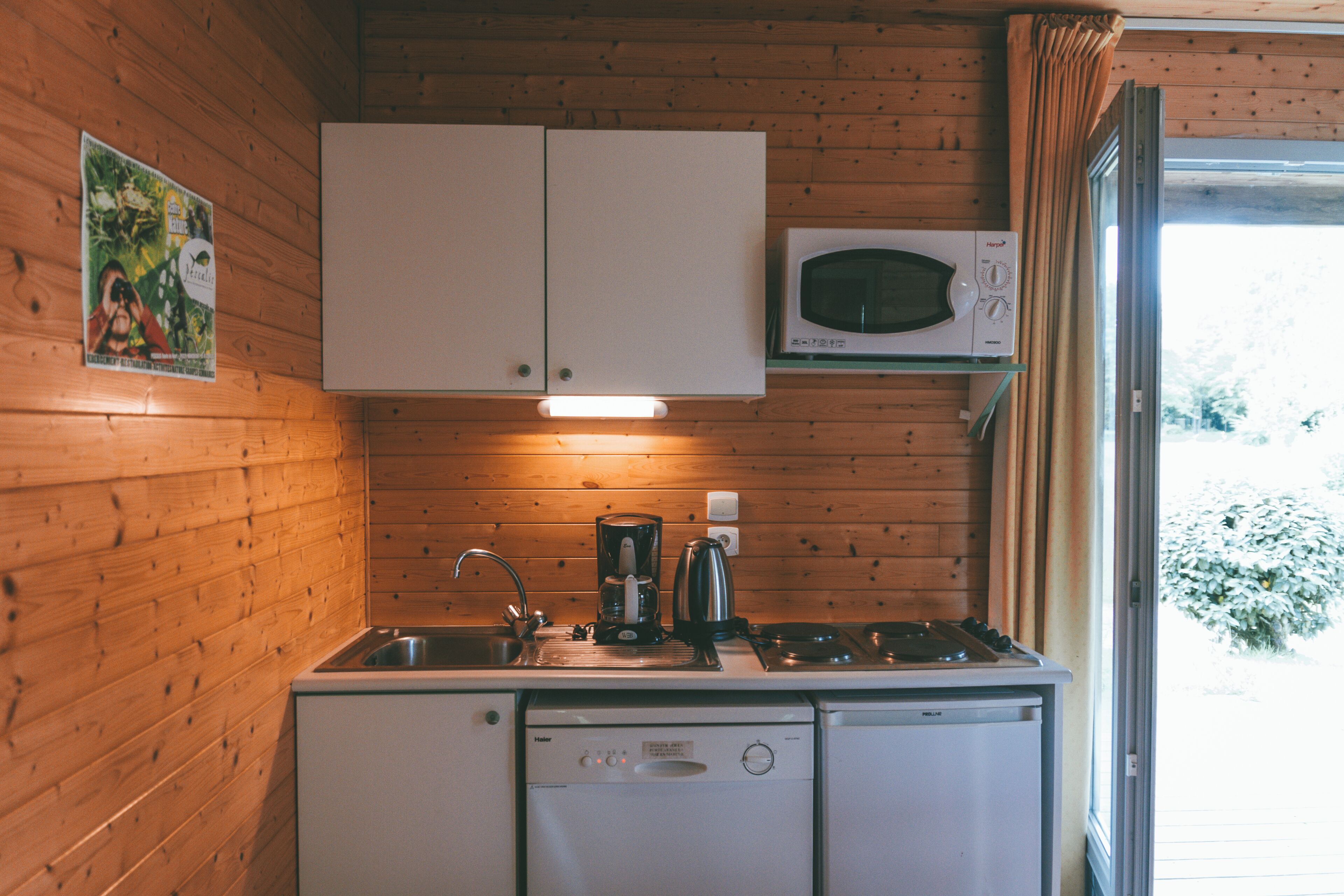 A compact kitchen with wooden walls, a microwave, a coffee maker, and a dishwasher.