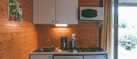 A compact kitchen with wooden walls, a microwave, a coffee maker, and a dishwasher.