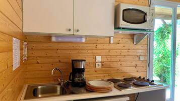 Une cuisine compacte aux murs en bois, dotée d’un four à micro-ondes encastré, d’une machine à café et d’un évier.