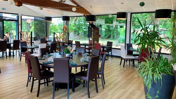 A spacious restaurant with wooden floors, large windows, and modern furniture.