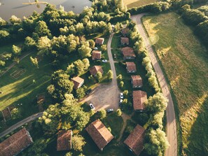 An aerial view of a residential area with multiple houses, a road, and a body of water in the background. - Terres de France - Natura Resort Pescalis (Moncoutant-sur-Sèvre)