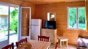 A wooden cabin with a dining area, a refrigerator, a television, and a window with curtains.