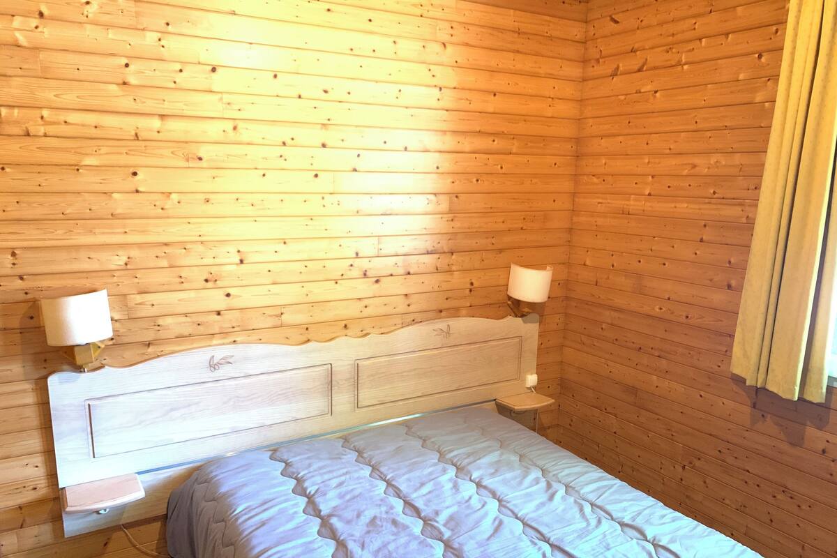 A wooden-paneled room with a bed, two bedside lamps, and a nightstand.