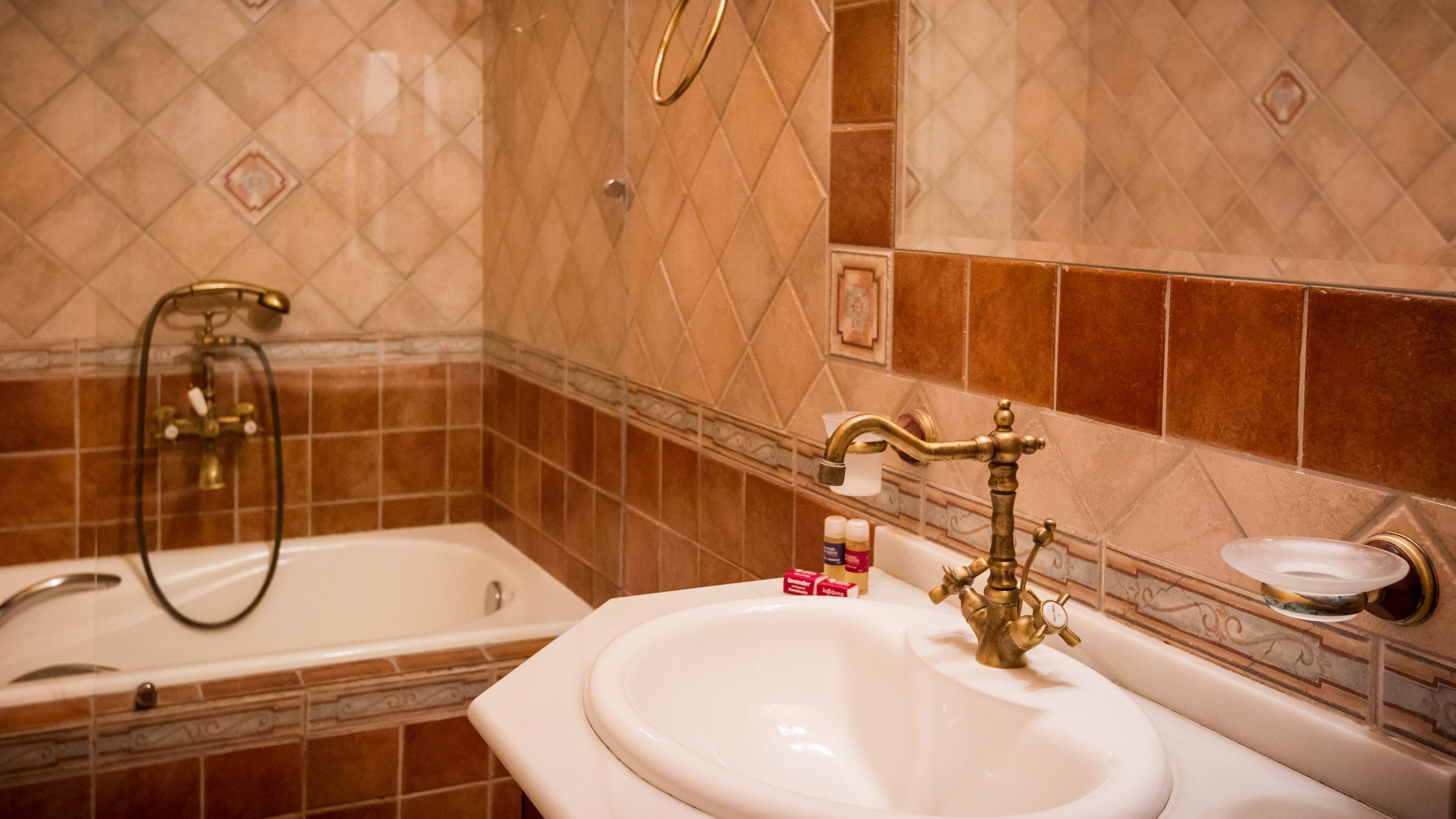 A bathroom with a bathtub, a sink with a gold faucet, and toiletries on the counter.