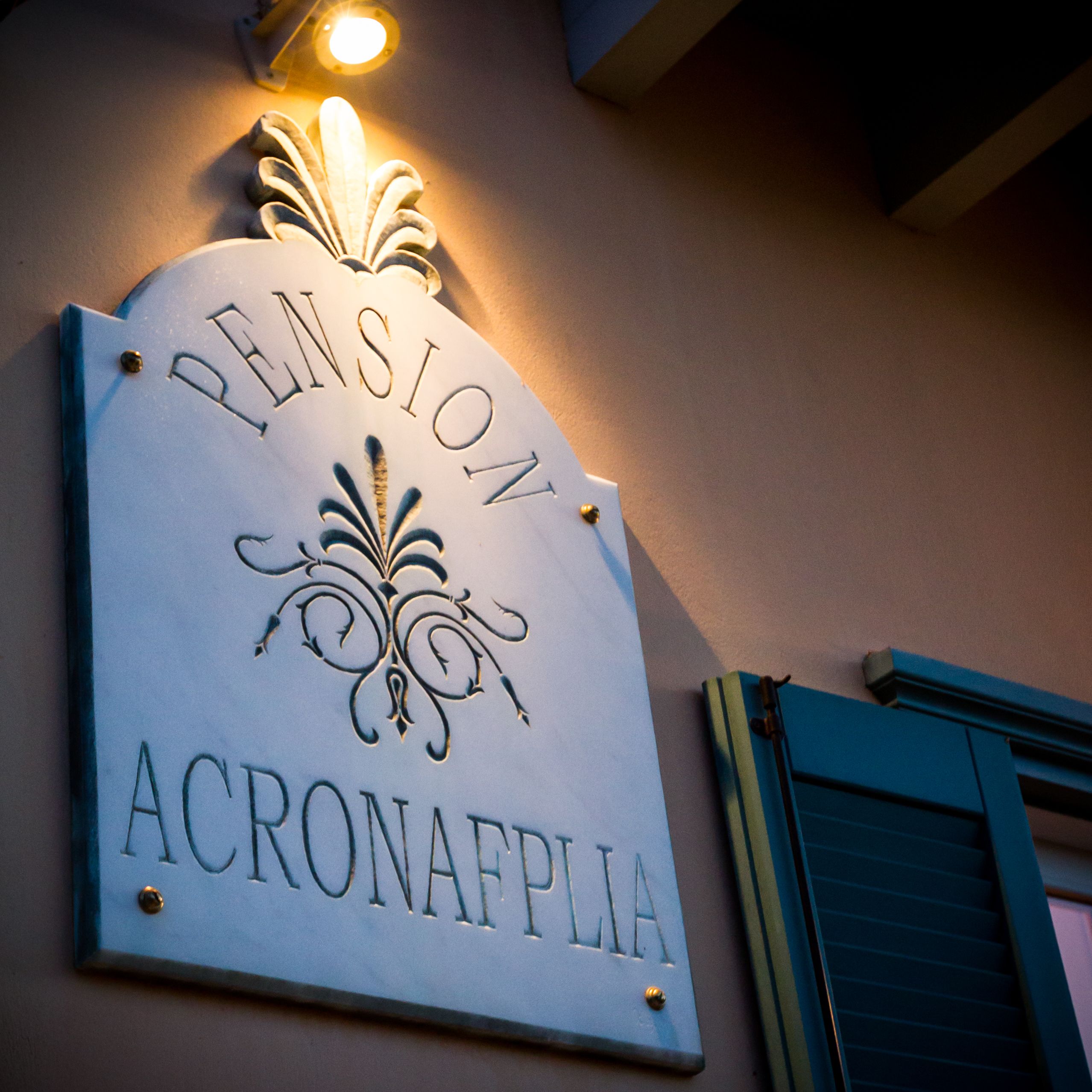 A sign for "Pension Acconaflia" with a decorative emblem and a light fixture above it.