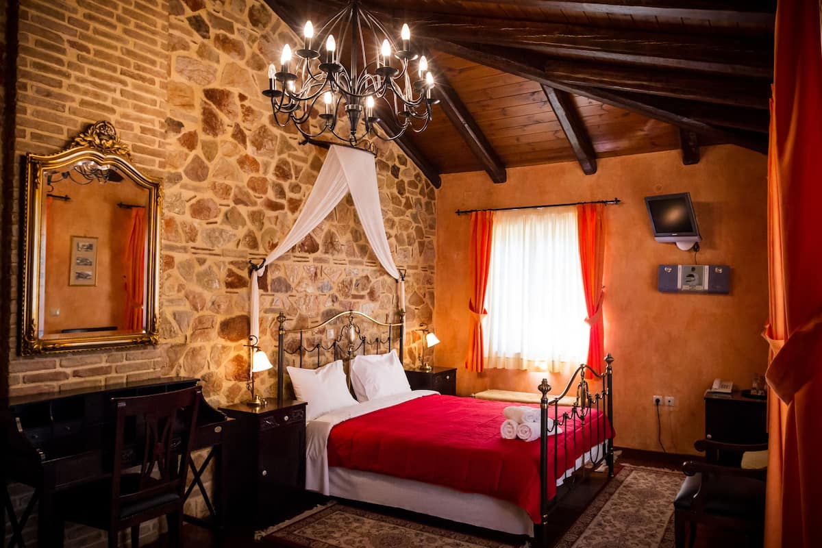 A bedroom with a stone wall, a four-poster bed, a chandelier, a television, and a desk with a chair.
