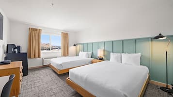 Quarto de hotel com duas camas, uma escrivaninha, uma cadeira, um abajur e vista para a cidade.