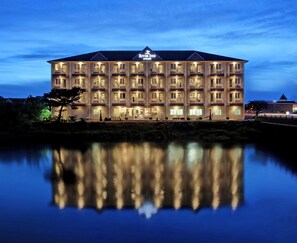 A multi-story hotel with a reflective pool in front, featuring balconies and a prominent sign at the top. - River Inn at Seaside (Seaside)