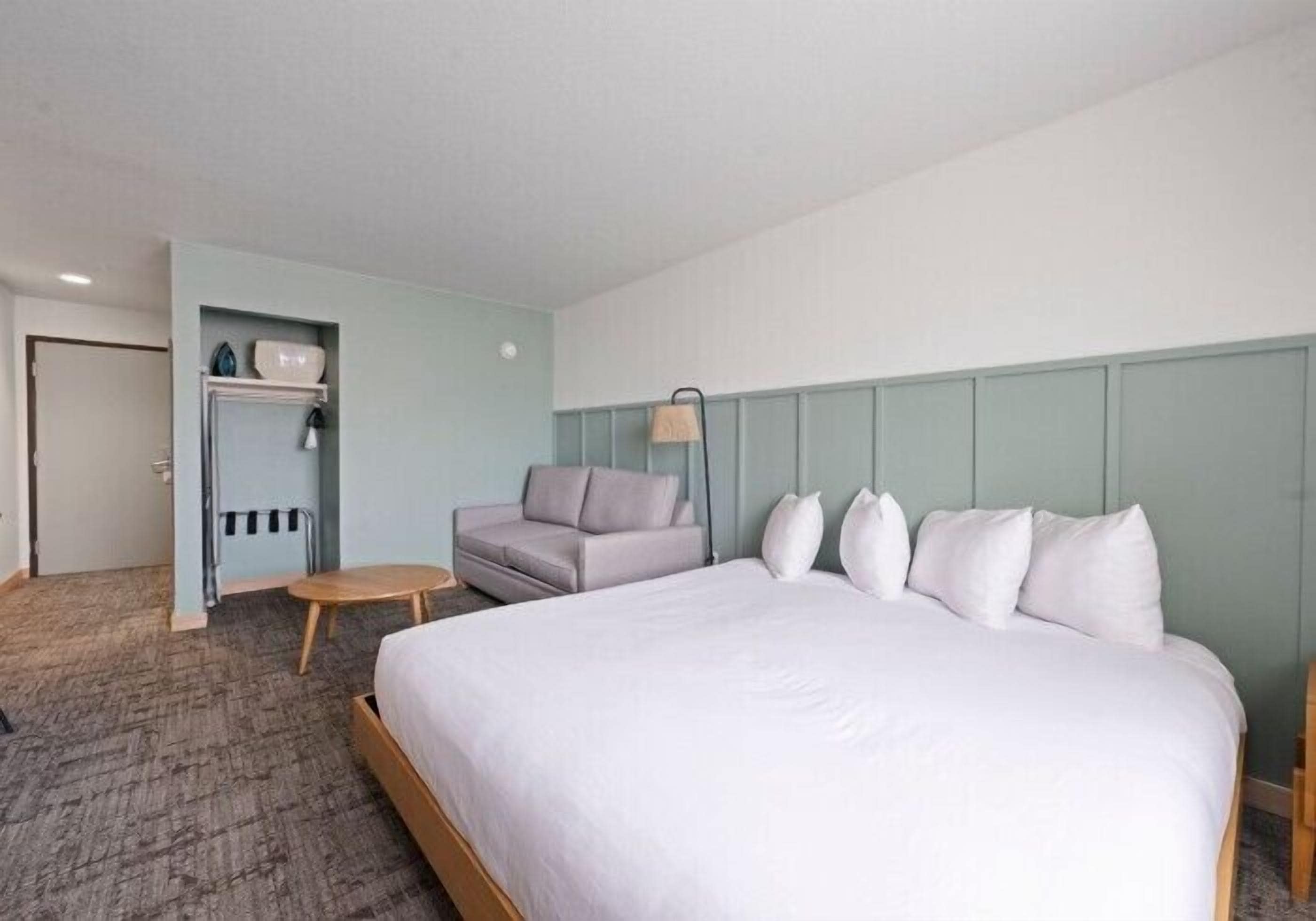 Une chambre d’hôtel comprenant un lit, un canapé, une petite table et une étagère fixée au mur, sur laquelle sont posés divers objets.