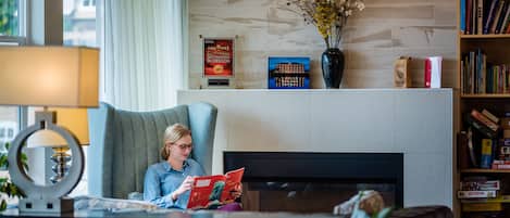 Une chambre d’hôtel avec un grand fauteuil, une cheminée, une bibliothèque et un vase rempli de fleurs.
