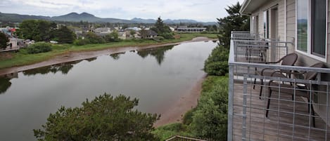 Uitzicht op een rivier vanaf een balkon met een metalen hekwerk, een houten terras en tuinmeubilair.
