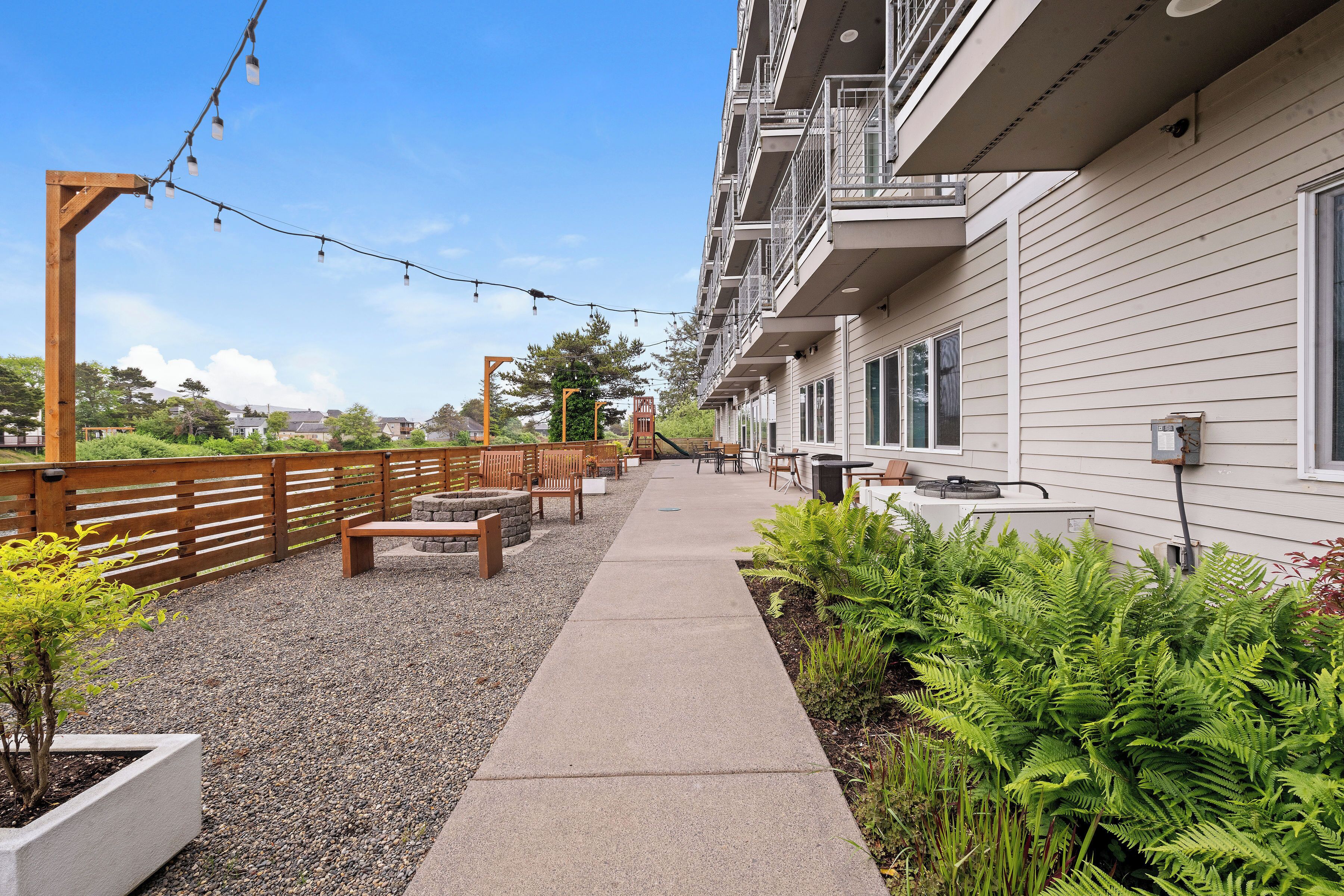 Un chemin menant à un bâtiment doté d’une terrasse et agrémenté de verdure.