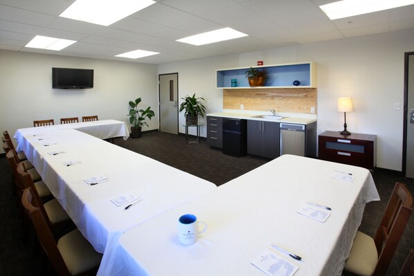 A conference room with a long table, chairs, a television, a kitchenette, and a small table with a lamp. - River Inn at Seaside (Seaside)