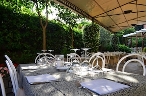 An outdoor dining area with tables set for a meal, surrounded by lush greenery and a covered seating area. - Albergo Ristorante Giardino (Cernobbio)