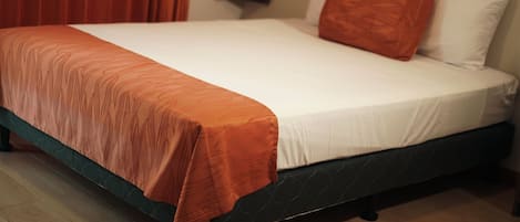 A bed with a white mattress and an orange bedspread, a dark headboard, and a red curtain in the background.