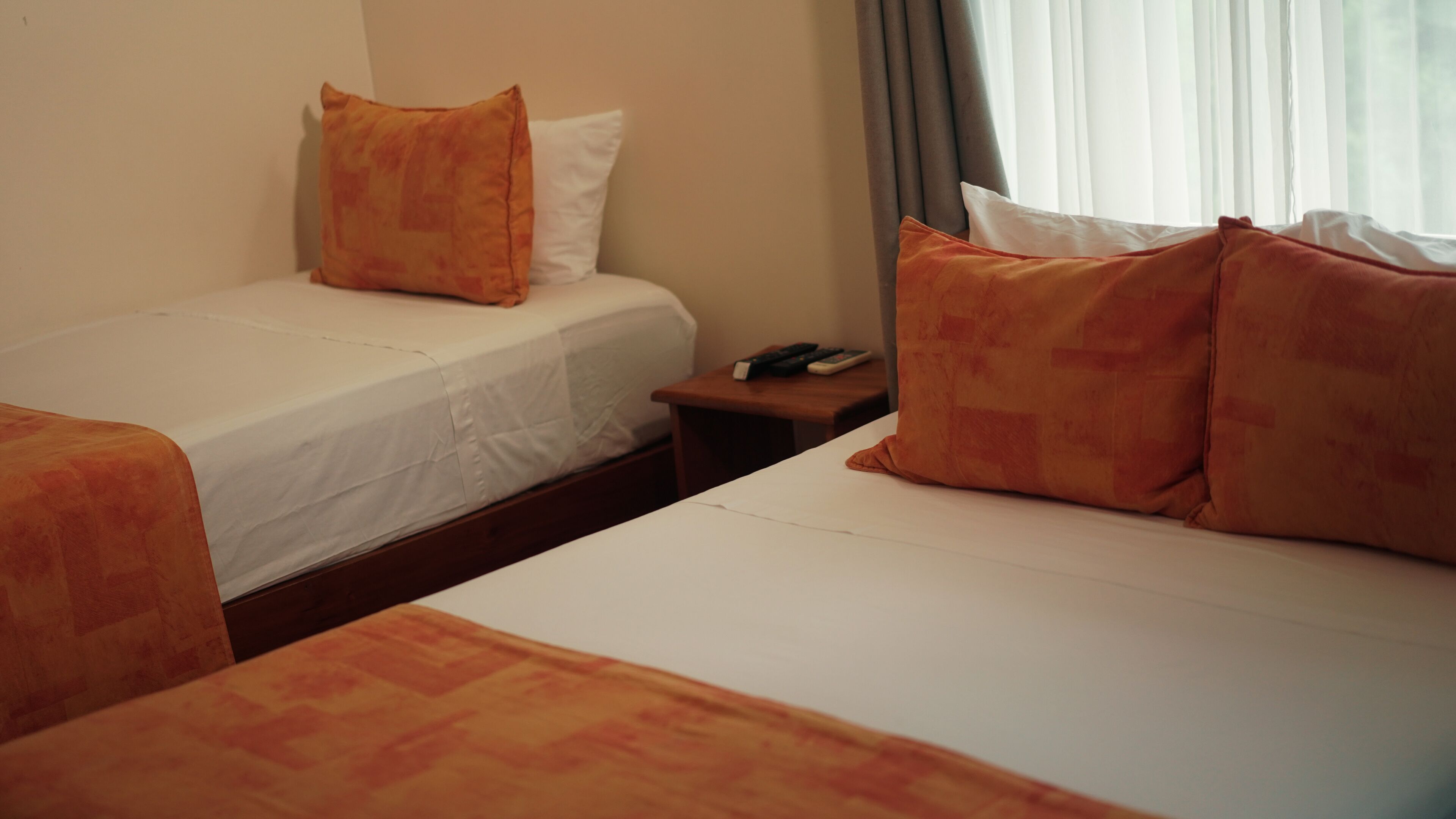 A hotel room with two beds, each with an orange bedspread and white pillows. There is a wooden nightstand with a telephone and remote controls.