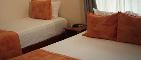 A hotel room with two beds, each with an orange bedspread and white pillows. There is a wooden nightstand with a telephone and remote controls.