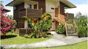 Una casa a due piani in legno con un balcone, una scala e un giardino pieno di fiori rosa.