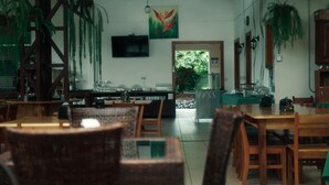 Un ristorante con tavoli e sedie in legno, un televisore appeso al muro e piante pensili.