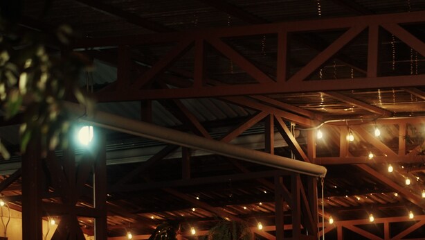 Zona pranzo all'aperto con sedie e tavoli in vimini, una struttura in legno a pergola e luci decorative.
