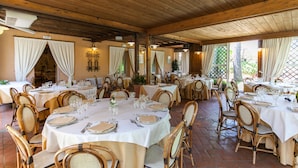 A restaurant with multiple tables set for dining, wooden ceiling beams, and white curtains. - Locanda Antiche Macine (Santarcangelo di Romagna)
