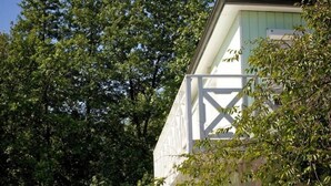 Een wit gebouw met een balkon, omgeven door weelderige groene begroeiing.