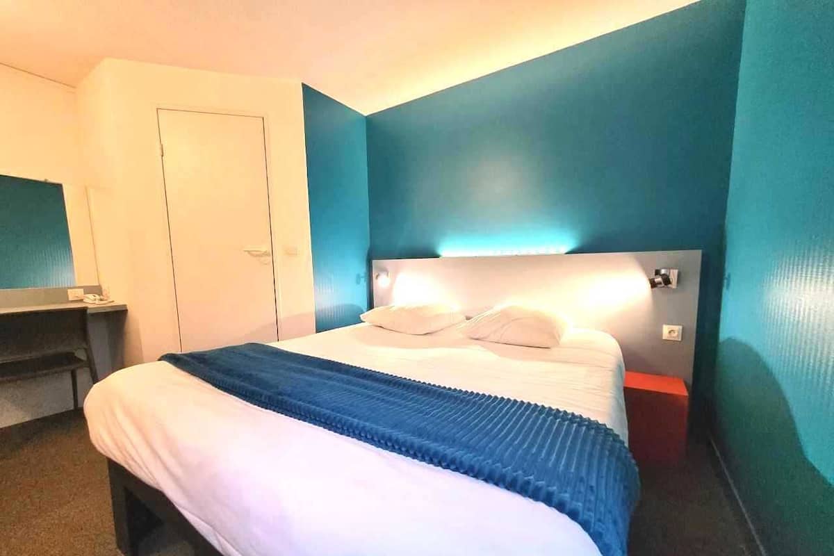 Una habitación de hotel con cama, mesita de noche y una puerta.