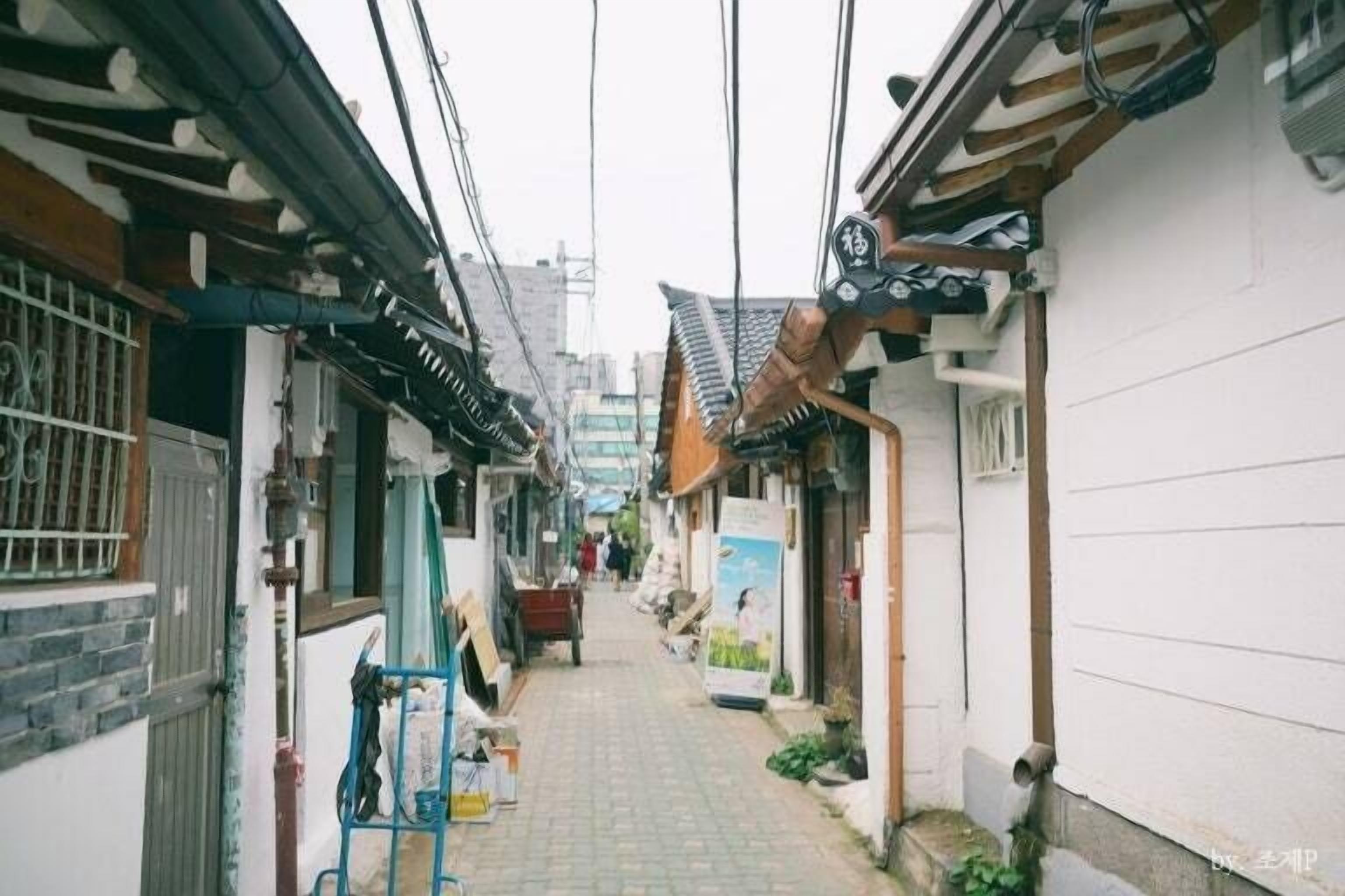 A narrow alleyway with traditional Korean architecture, including tiled roofs and wooden beams.