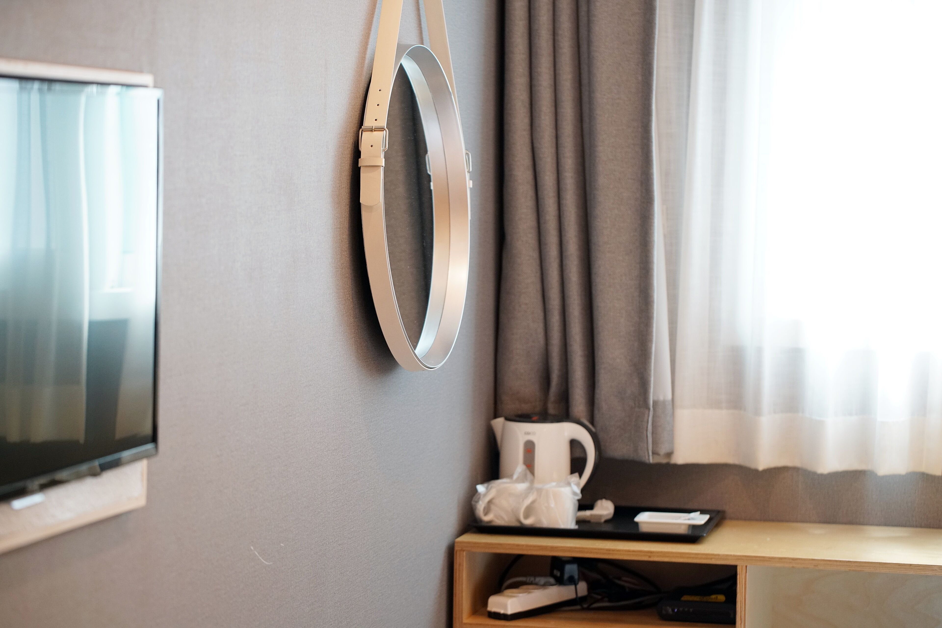 A hotel room with a flat-screen TV mounted on the wall, a white coffee maker on a wooden table, and a remote control on the table.