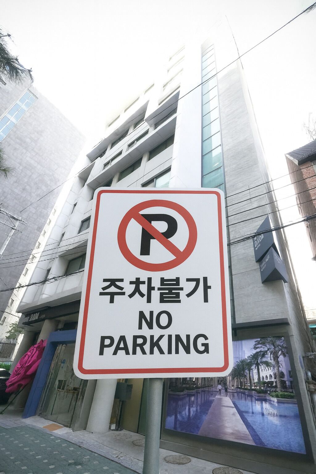 Un panneau «interdiction de stationner» devant un bâtiment moderne doté de grandes fenêtres, avec une piscine visible à l’arrière-plan.