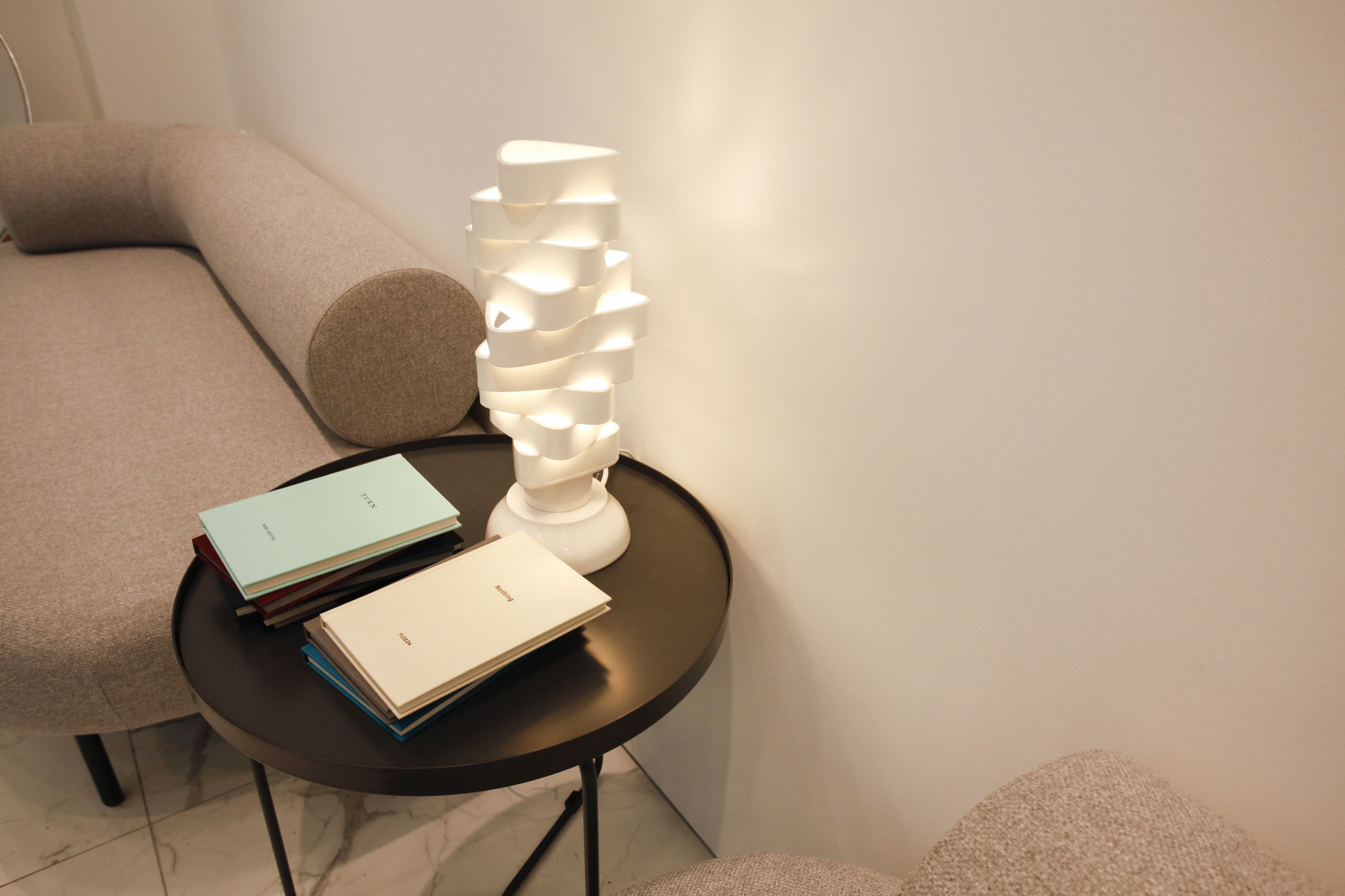 A small round table with a modern lamp and a stack of books.