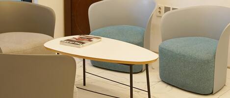 A room with a marble-tiled floor, a wooden cabinet with glass doors, two grey armchairs, and a small white table with a magazine.