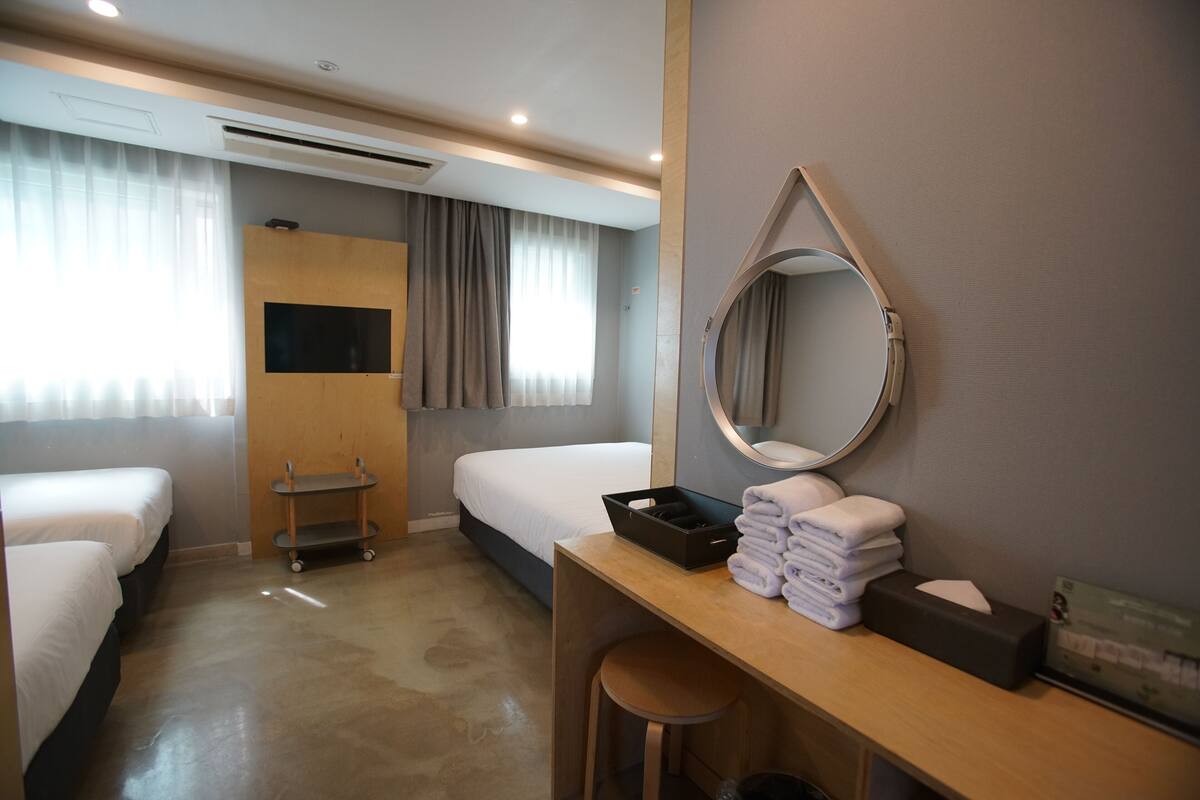 A hotel room with two single beds, a desk with a mirror, a small table, and a TV.
