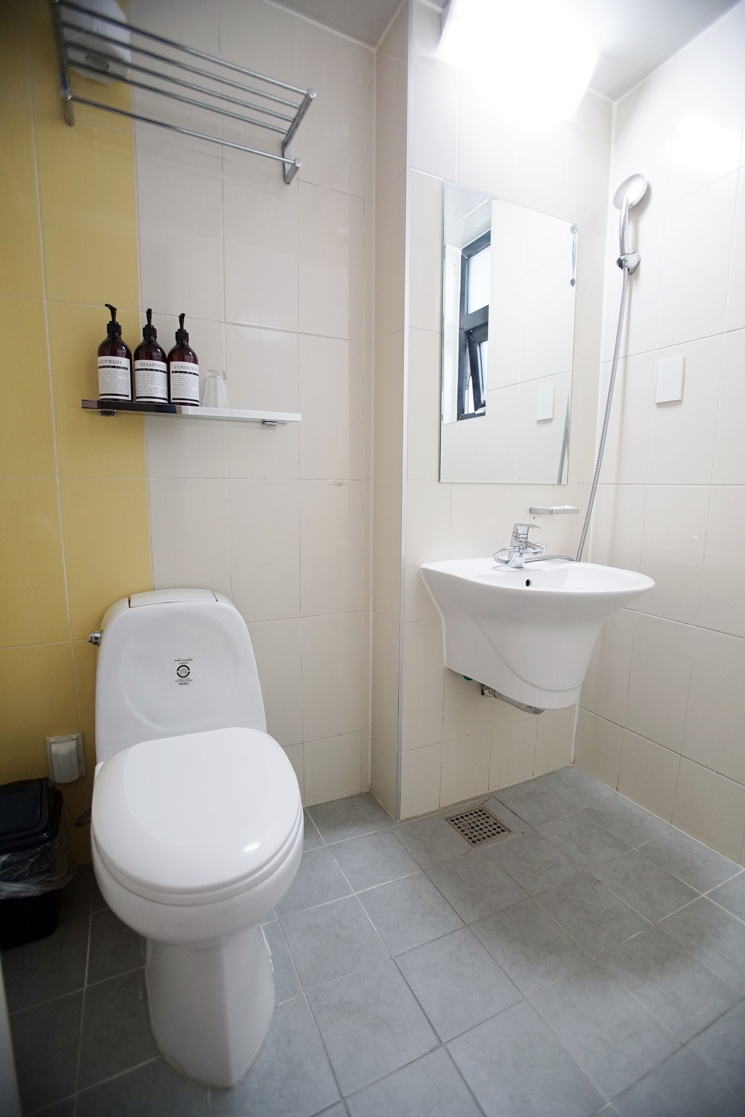 A bathroom with a toilet, sink, and shower. There are toiletries on a shelf.