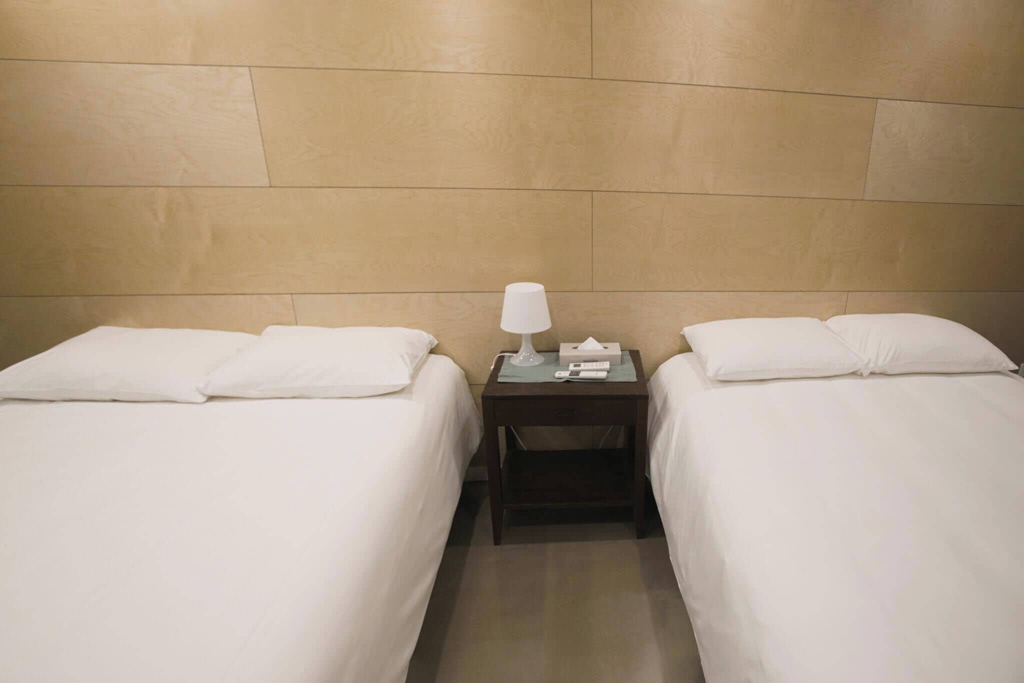 A hotel room with two single beds, a nightstand with a lamp, and a box of tissues.