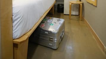 A compact hotel room with a single bed, a desk with a computer, a small table, a mirror, and a suitcase.