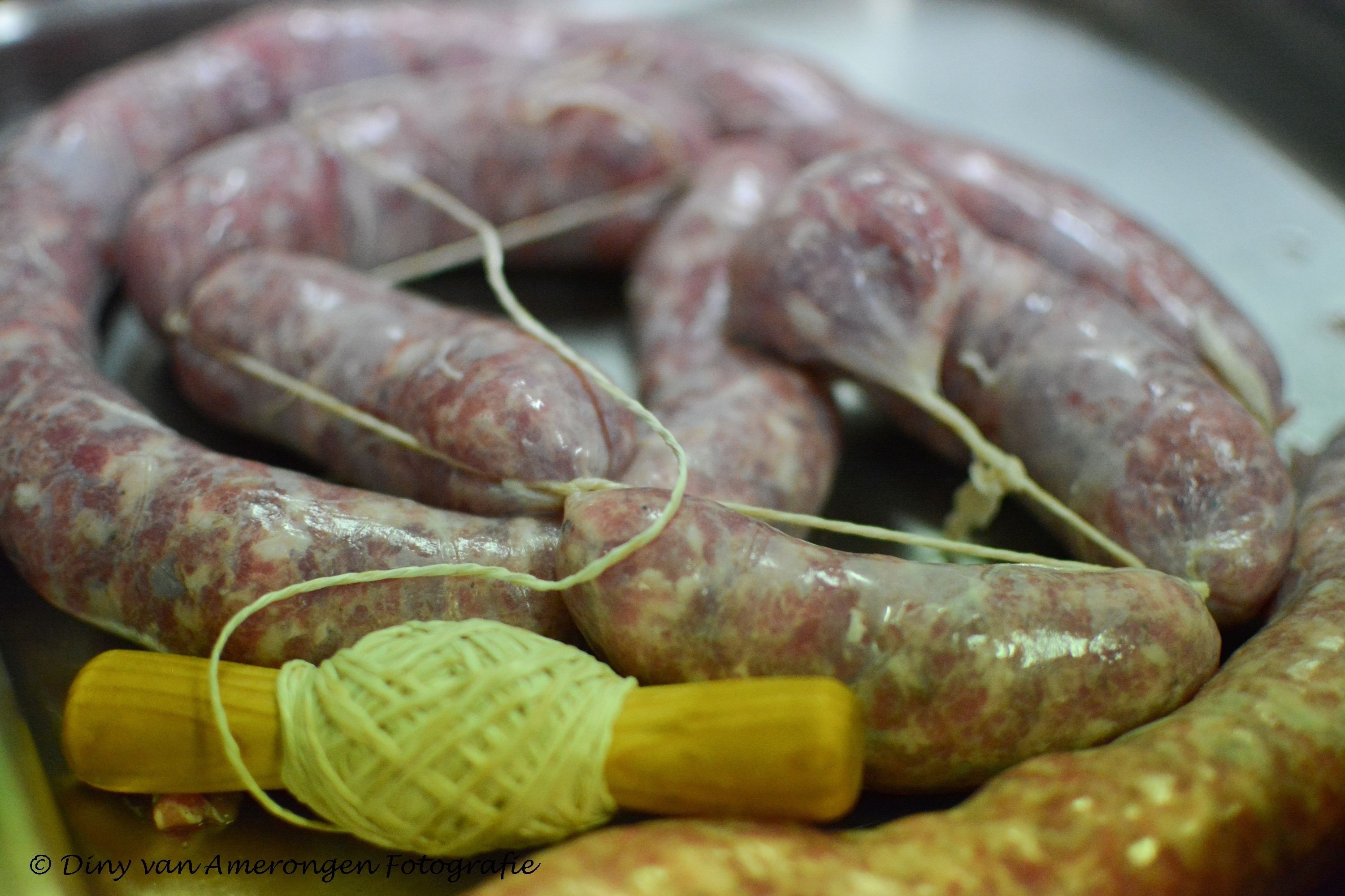 A close-up of raw sausages tied with string, with a wooden stick and a woven cloth nearby.