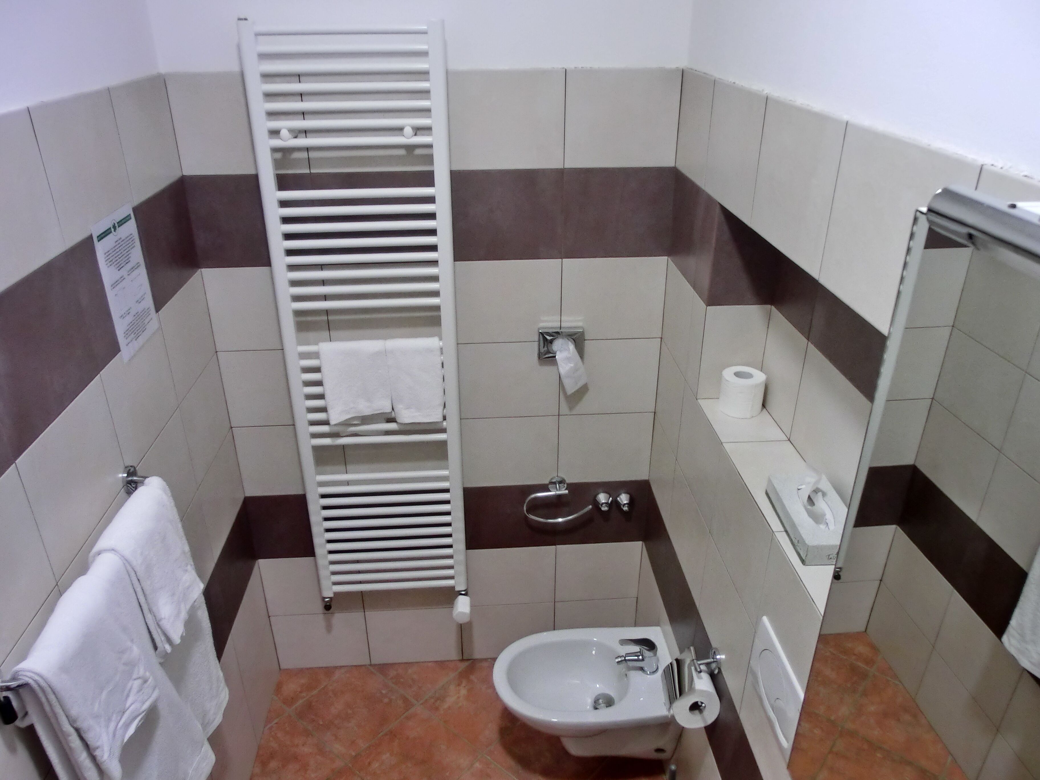 A small bathroom with a toilet, bidet, towel rack, and a paper towel dispenser.