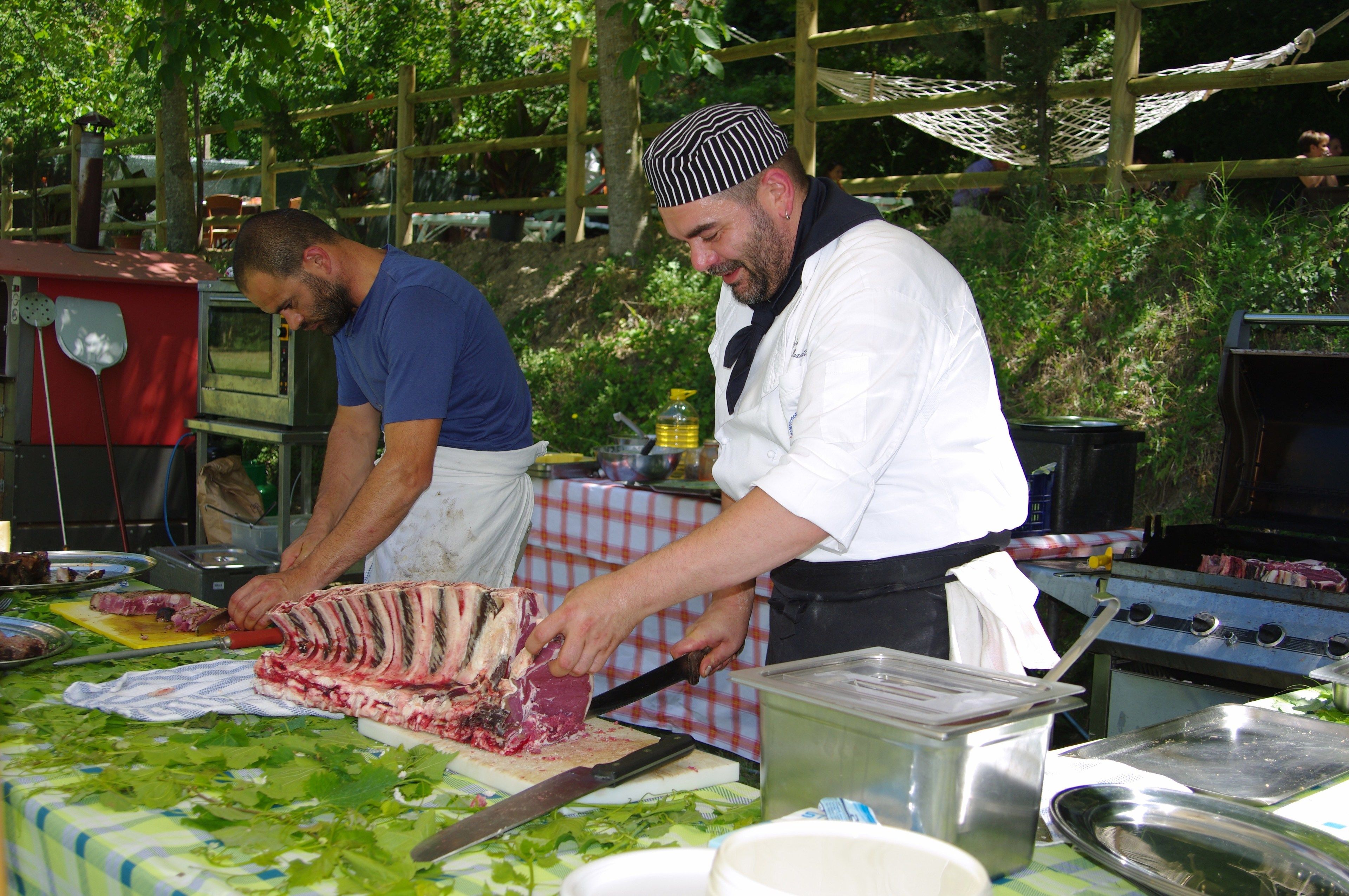 Ein Koch bereitet im Freien Essen mit einem Grill und Kochgeschirr zu.