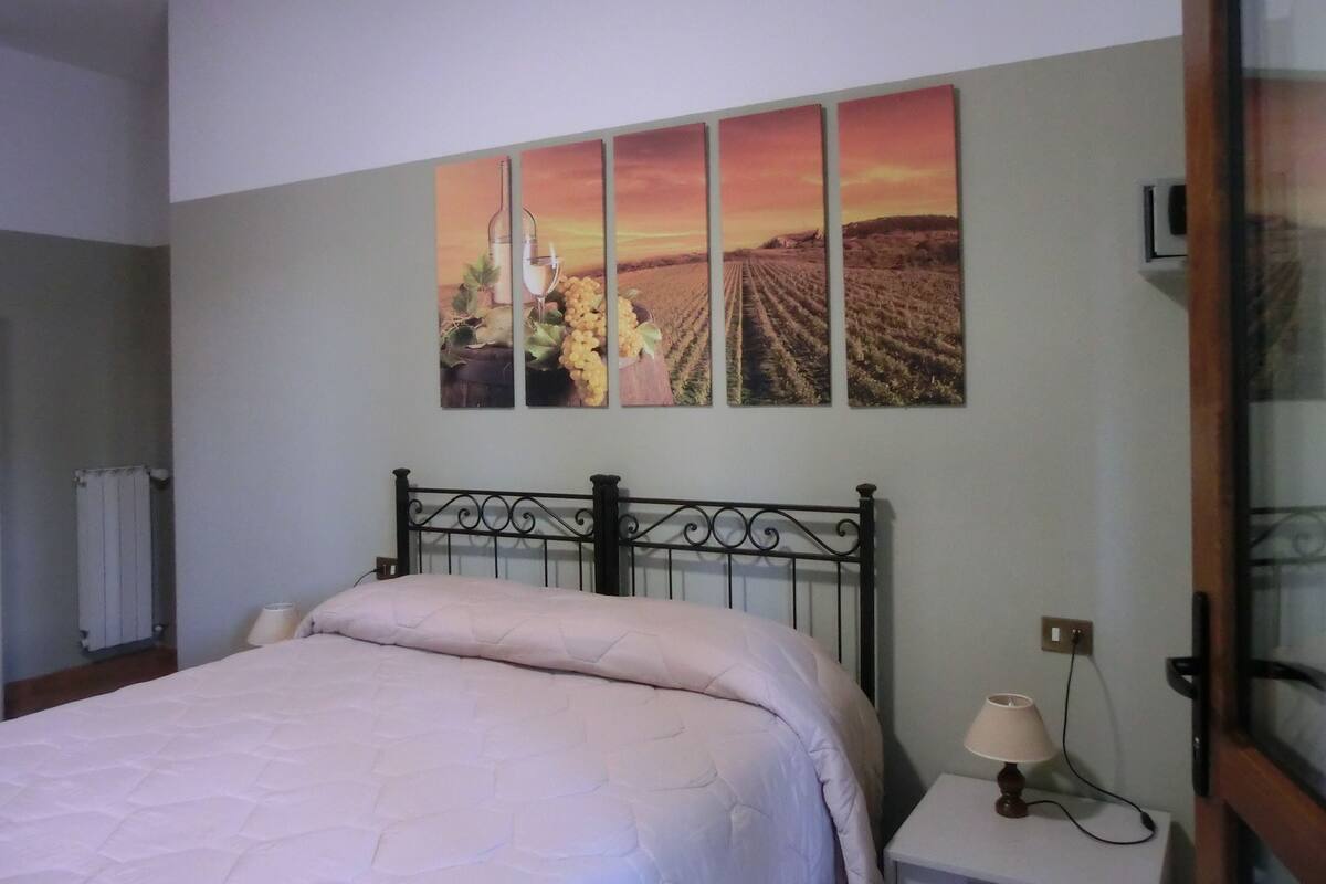 Un dormitorio con cama, mesita de noche, lámpara y una pared decorada con tres cuadros.