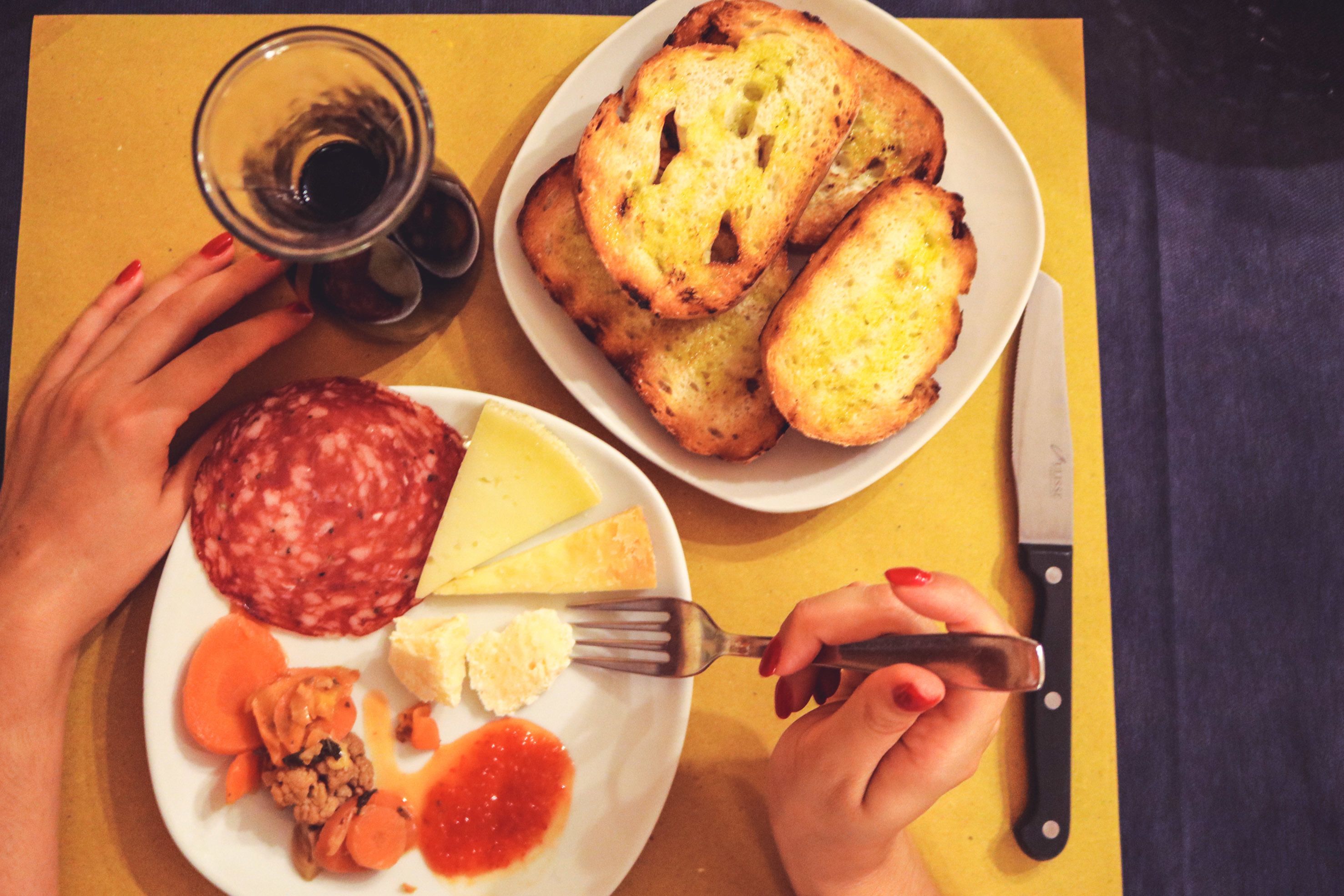 A table with a plate of food including bread, cheese, and a meat dish, a glass of drink, and a knife.