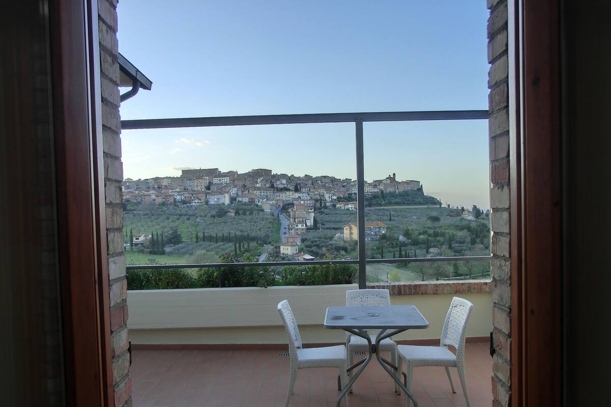 Un balcón con mesa y sillas, con vistas a un pueblo con edificios y vegetación.