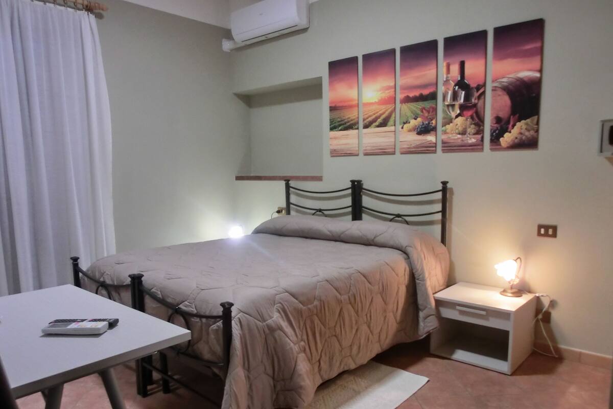 Un dormitorio con cama, mesita de noche, lámpara y aire acondicionado instalado en la pared.