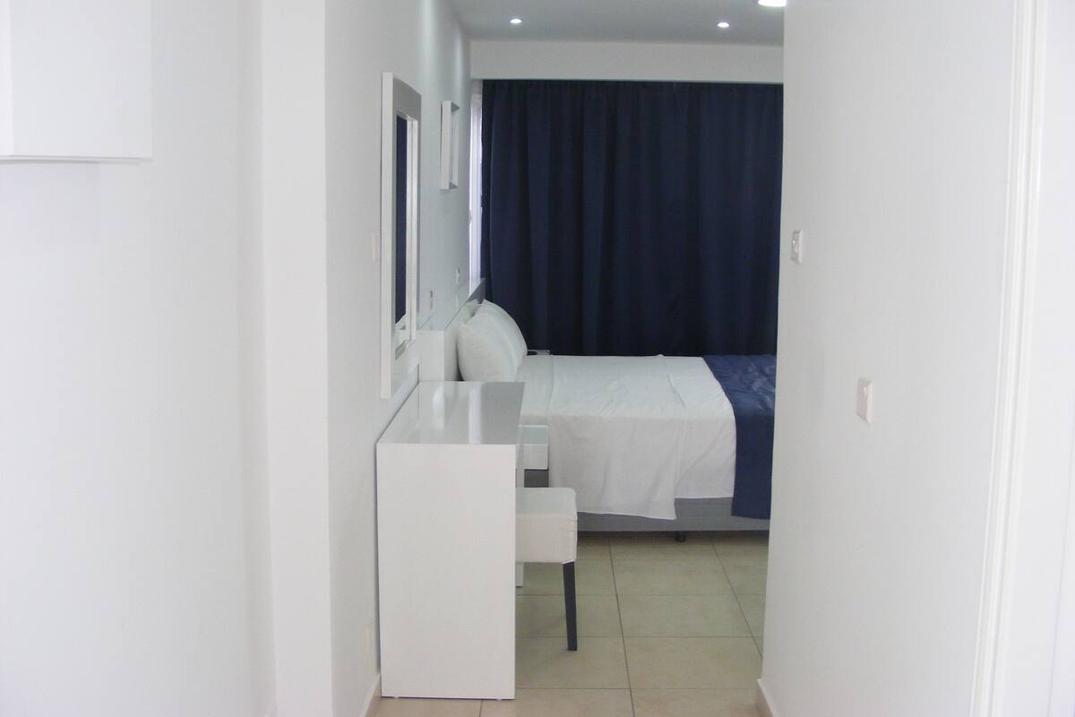 Un pasillo estrecho que conduce a un dormitorio con cama, mesita de noche y espejo.