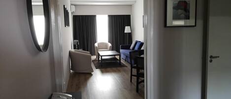 A hotel room with a wooden floor, a desk with a telephone, a chair, a sofa, and a dining table.